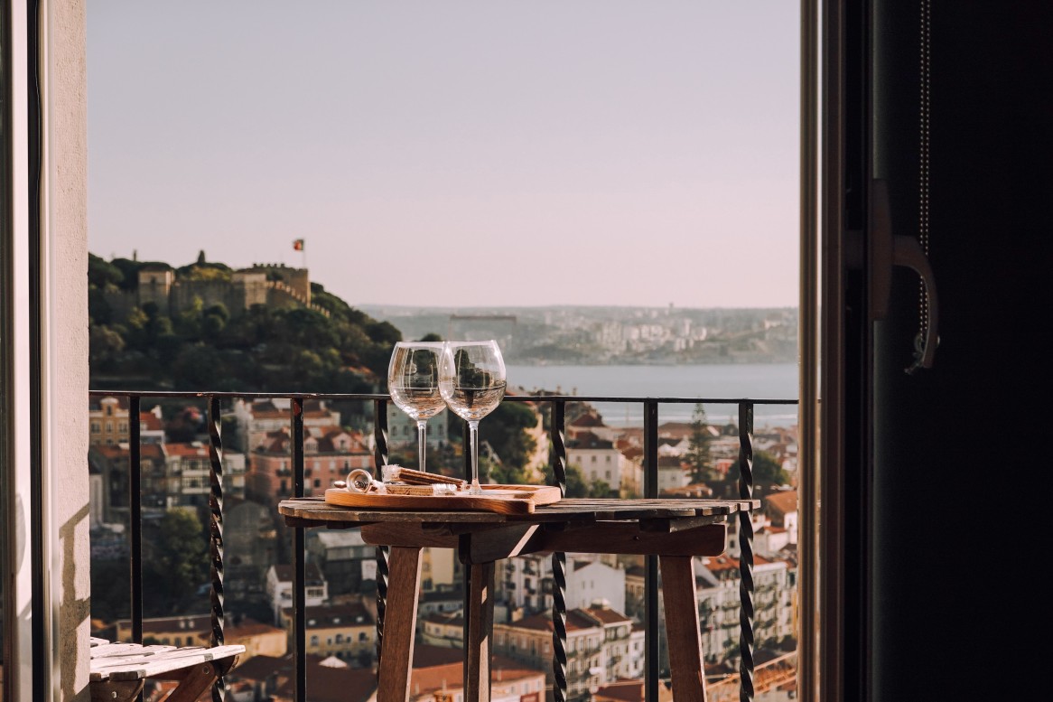 A balcony with two glasses of white wine on a table overlooking Lisbon