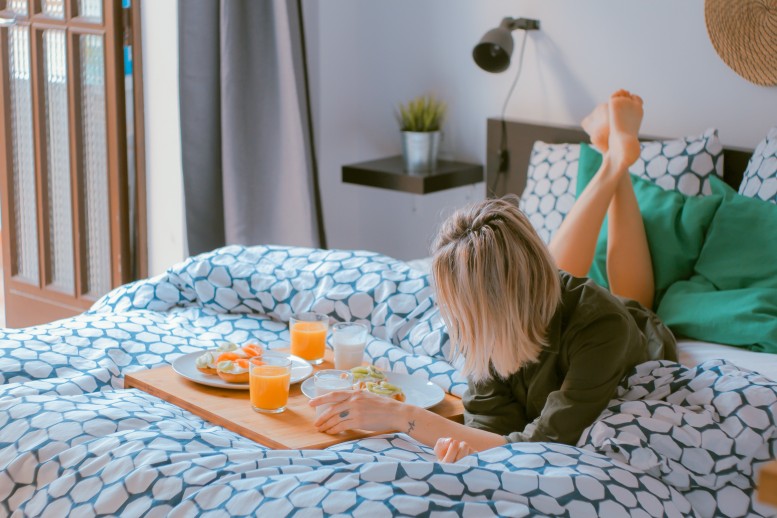 Woman eating breakfast on a bed with colourful sheets