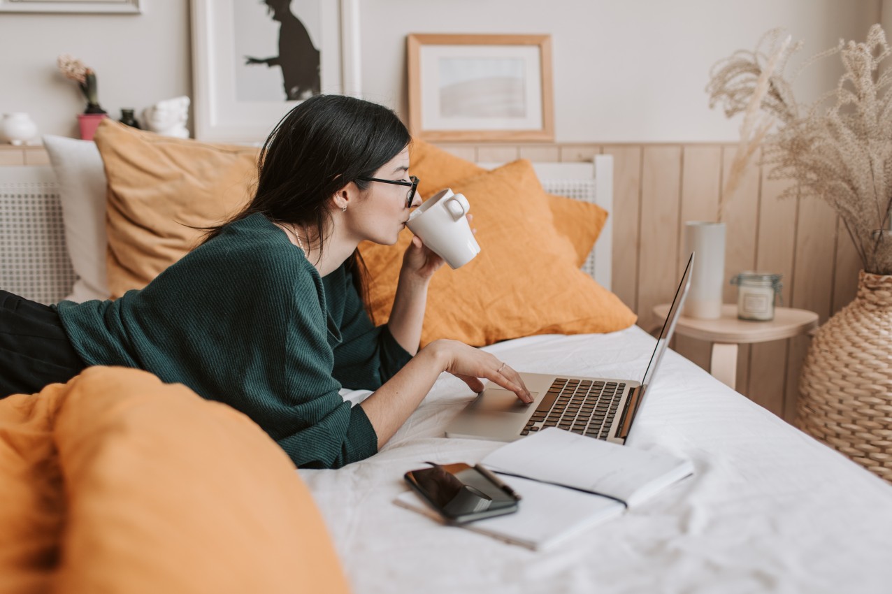 Woman sitting on bed with orange pillows using a laptop in uni bedroom.jpg
