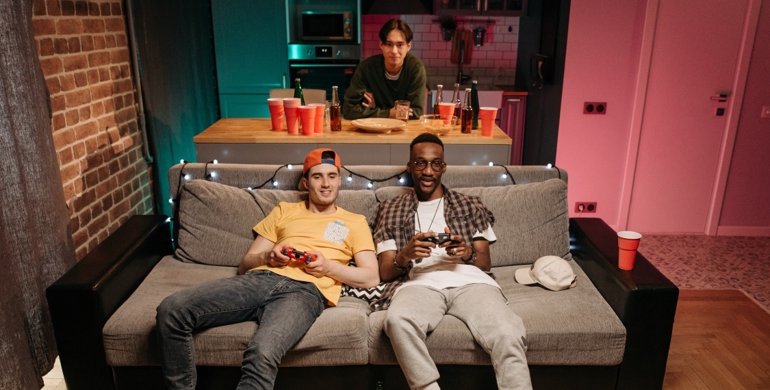 Two men sitting on a sofa playing games in a man cave