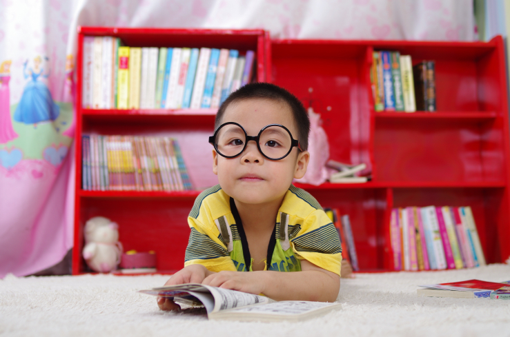 A boy reading a book in his nursery with a bookshelf in the background